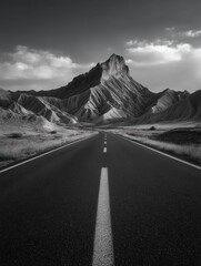 A black and white photograph of a long road leading into the horizon, with a mountain in the background.