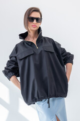 Elegant woman in black windbreaker jacket and light blue skirt on white background. Fashionable female style. Studio photography. Vertical photo. High quality photo © lara-sh