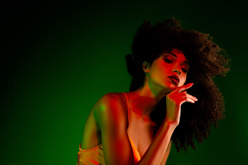 Stylish young woman with stunning curly hair in red and green lighting, posing with contemporary allure.