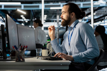 Programmer in data center using computer, doing software updates, verifying neural network parameters. Server room worker using PC to inspect configurations, ensuring optimal application performance