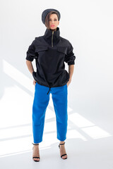 Elegant woman in black windbreaker jacket, blue pants and nautical hat on white background. Fashionable female in ocean French style. Studio photography. Vertical photo. High quality photo