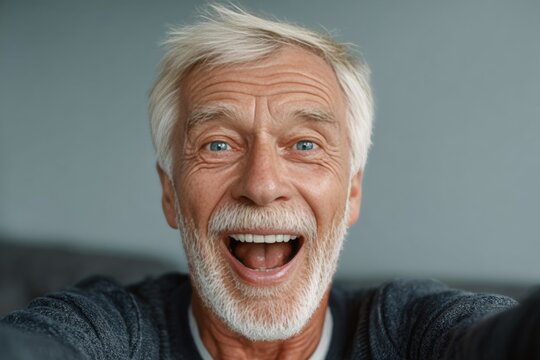 An older gentleman with a beard and mustache is joyfully posing for a selfie.