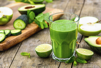 Glass of green detox smoothie with avocado cucumber lime and apple on rustic wooden background, healthy detox drink concept, copy space