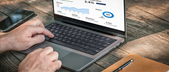 Entrepreneur using laptop to analyze traffic and user retention data. Modern business analytics workspace on wooden table with device and notebook