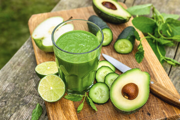 Glass of green detox smoothie with avocado cucumber lime and apple on rustic wooden background, healthy detox drink concept, copy space