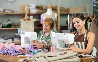 Elderly and young women seamstresses sewing on machine in sewing workshop