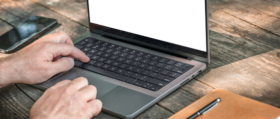 Closeup of male hands typing on laptop with blank screen on wooden table. Remote work concept