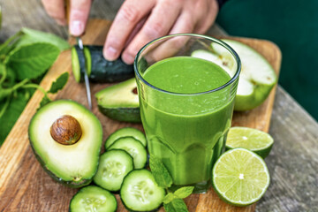 Glass of green detox smoothie with avocado cucumber lime and apple on rustic wooden background, healthy detox drink concept