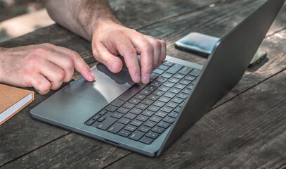 Closeup of male hands typing on laptop with blank screen on wooden table. Remote work concept