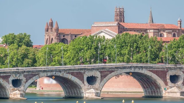 Garonne River and Pont Neuf timelapse with Basilica of Our Lady of the Daurade in downtown Toulouse, France. Renaissance arch bridge reflects in the water under a blue sky. Waterfront with green trees