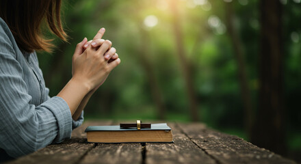 Woman Praying with Hands Clasped Over a Bible with a Cross Outdoors