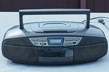 one old plastic portable with antenna stereo with speakers black with buttons on cassettes with handle electric with cd player tape recorder stands on gray table