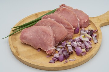 Raw pork steaks with sliced ​​red onion and green onion on wooden board ready to cook