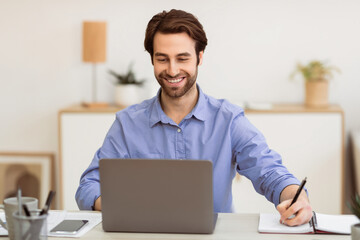 Cheerful Businessman Writing Taking Notes Working On Laptop Sitting At Workplace In Modern Office. Successful Business Career, Entrepreneurship Concept. Selective Focus