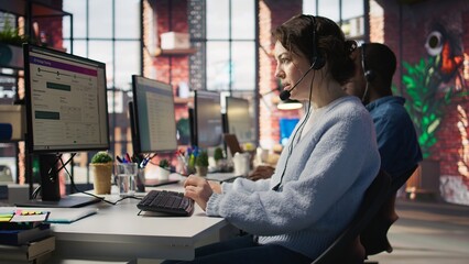 Call center team of agents wearing headset assisting customers over phone at modern workstation with multiple monitors, emphasizing customer support, communication and service efficiency, camera B