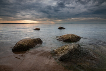 serene lake shore with boulders at sunset under dramatic cloudy sky