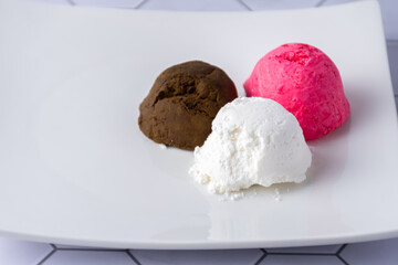 Three bowls of colored ice cream in a square dish on a table.