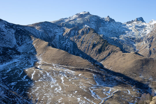 Vista mozzafiato di una catena montuosa con pendii innevati e rocce a vista sotto un cielo azzurro e terso. Fotografia paesaggistica ideale per temi naturali e stagionali.