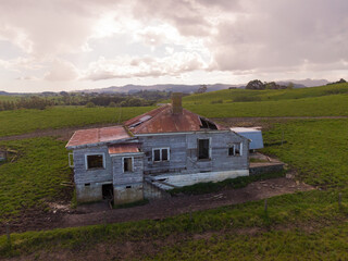 Obraz premium A decaying abandoned house with a rusty roof stands on a green rural hillside, a symbol of neglect and the passage of time. Matakana, Warkworth, Auckland, New Zealand