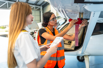 Aircraft maintenance engineer inspecting airplane wing with pilot in hangar