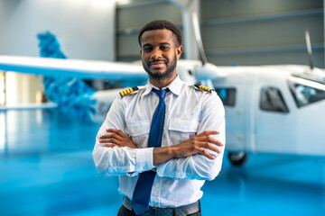 Confident african american pilot posing with arms crossed in aircraft hangar © unai