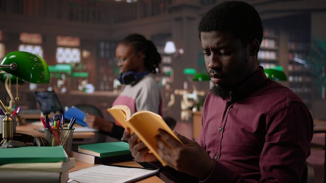African american guy studies for a critical law exam and reading specialty books to complete class notes with reliable academic information. Studying in the library before the test. Camera B.