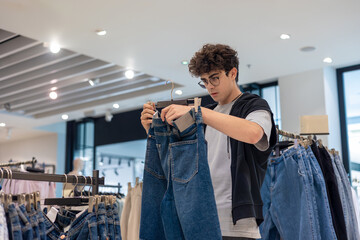 Teenager holding shorts while shopping in clothing store. Young customer shopping trendy casual wear at fashion retail shop. Teenage consumer making fashion choices. Boy shopping alone. Copyspace