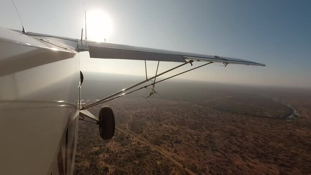 Aerial wide of small air plane side view flying over dry savannah with shrubs, river and road in a sunny morning in Kenya