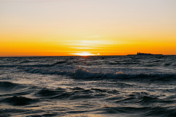 Ocean with waves, sunset sky is orange. water is choppy and waves are crashing on shore. beauty in nature, wild sandy beach at sunset. vacation or travel.