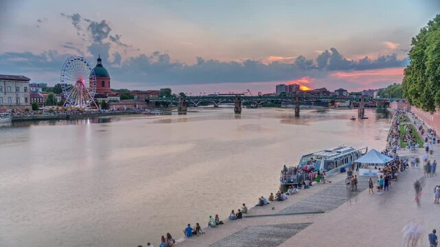 Aerial view of La Grave Hospital with Saint-Pierre Bridge. Port de la Daurade park along the Garonne River timelapse in Toulouse, France. Sunset colorful clouds, ferry at dock and riverside atmosphere