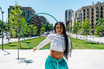 Young woman dancing with hula hoop in urban park, promoting healthy lifestyle and fitness