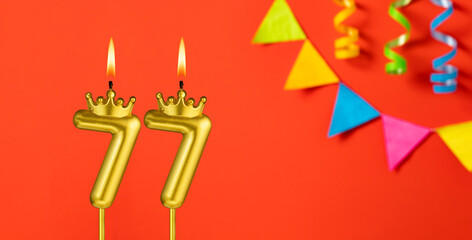 Number 77 candle - Birthday celebration on an orange background with pennants