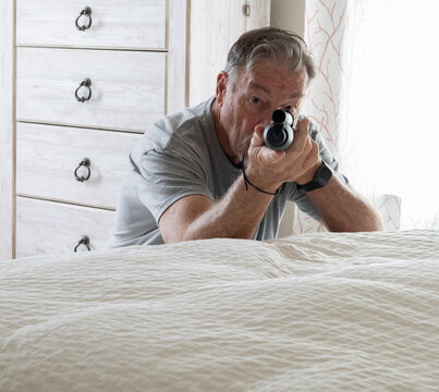 A senior citizen is protecting himself with a shotgun from an intruder in his bedroom while calling the police on his cell phone
