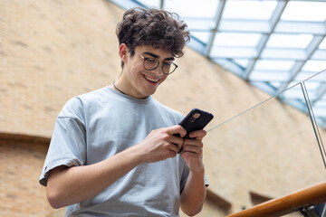 Smiling teenage boy using smartphone in modern urban space. Concept of youth lifestyle, digital...