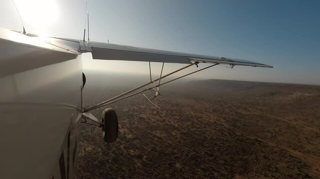 Aerial wide of small air plane side view flying over dry savannah with shrubs and road in a sunny morning in Kenya
