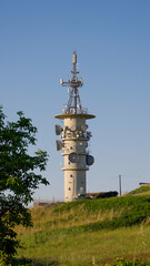 Obraz premium Telecommunication tower with antennas and satellite dishes standing on a hill and transmitting data under blue sky