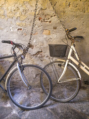 Two vintage bicycles chained to a weathered wall, capturing the rustic charm and everyday life of an old European town. A timeless scene of simple living