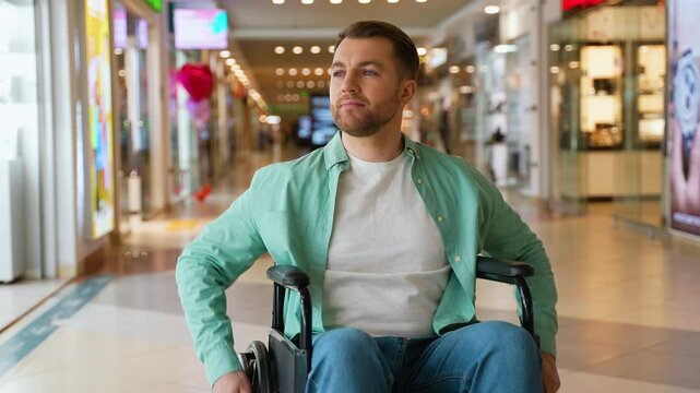 Portrait of a smiling handsome man sitting in wheelchair moving in shopping mall