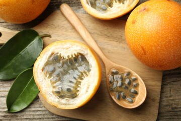 Ripe passion fruits, seeds and green leaves on wooden table, flat lay