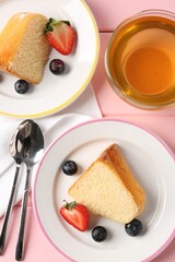Pieces of tasty bundt cake with berries and tea on pink wooden table, flat lay