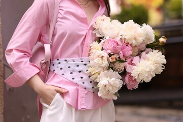 Stylish woman with beautiful peonies on city street, closeup © New Africa