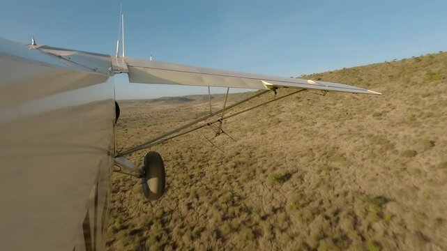 Aerial wide of small air plane side view flying low over dry savannah with shrubs and hills in a sunny morning in Kenya