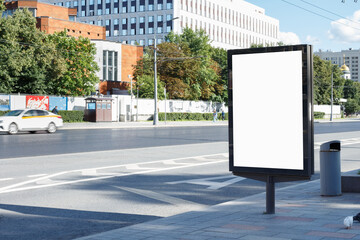 Vertical blank white billboard on a city street. Bright sun, clouds. Mock-up.
