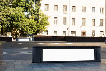 Horizontal billboard on the building envelope. Green trees and an old building are brightly lit by the sun. Mock-up.