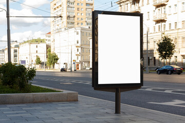 Blank vertical billboard, highway. Bright sun illuminates city buildings. Mock-up.