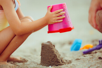 Child Makes Sand Castles on the Beach at Sea. Little girl building sandcastles by the seaside with her dad
