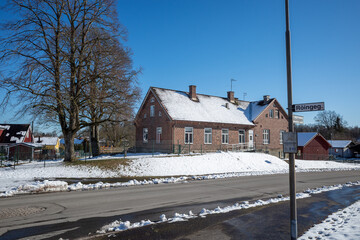 Old Roinge school building with snow-covered roof, a street sign, and winter landscape in Haessleholm, Sweden