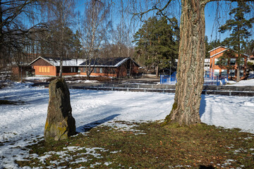 Linneskolan school buildings, large trees, and ancient runestone on a snowy winter day in Haessleholm, Sweden