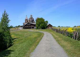 An old wooden fence around a field with meadow flowers and Church of the Transfiguration of the Lord built in 1714 on Kizhi Island in Karelia