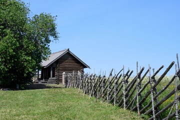 An old wooden house and fence around a field with meadow flowers on Kizhi Island in Karelia